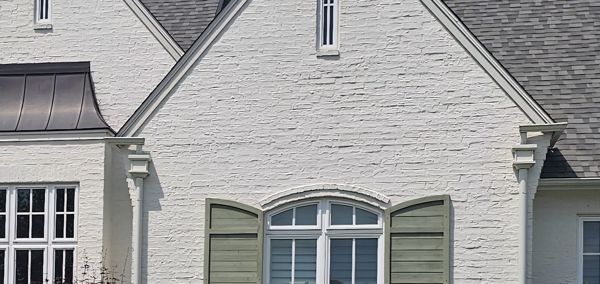 Architectural detail of white brick home with green shutters by My Roofing